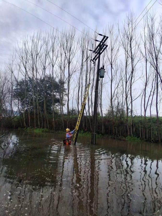 Técnico en una escalera junto a un poste, con el terreno inundado